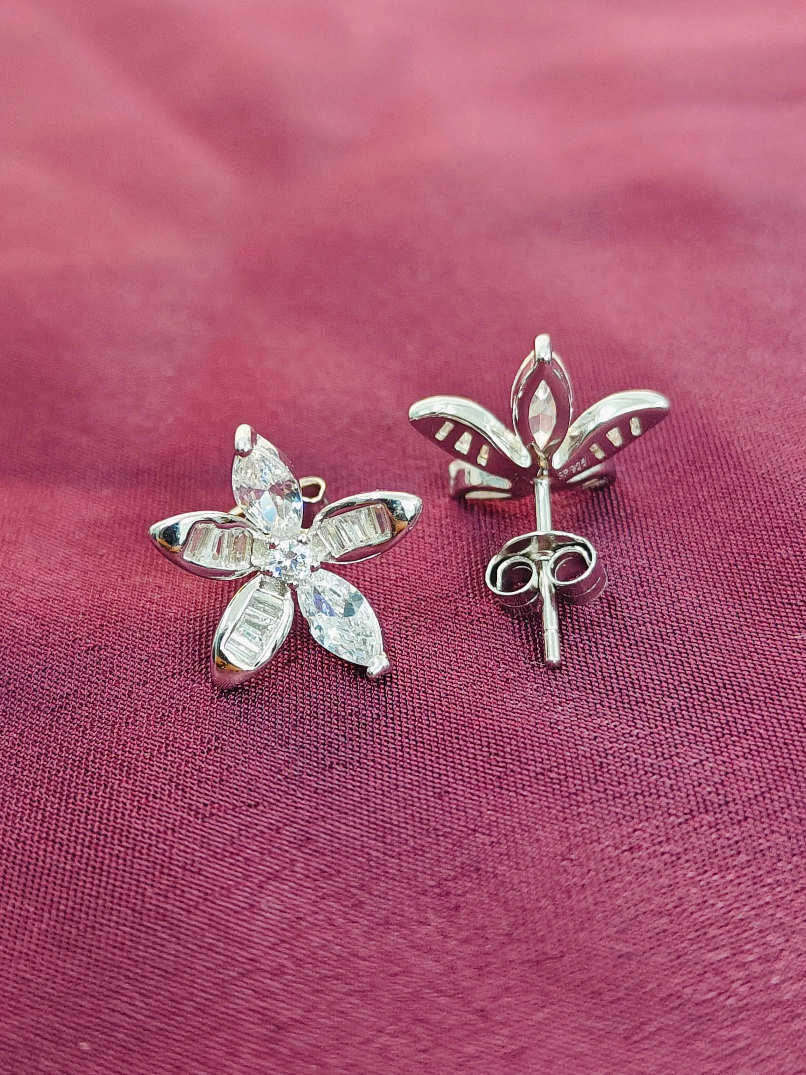 Silver butterfly-shaped earrings on a pink fabric background